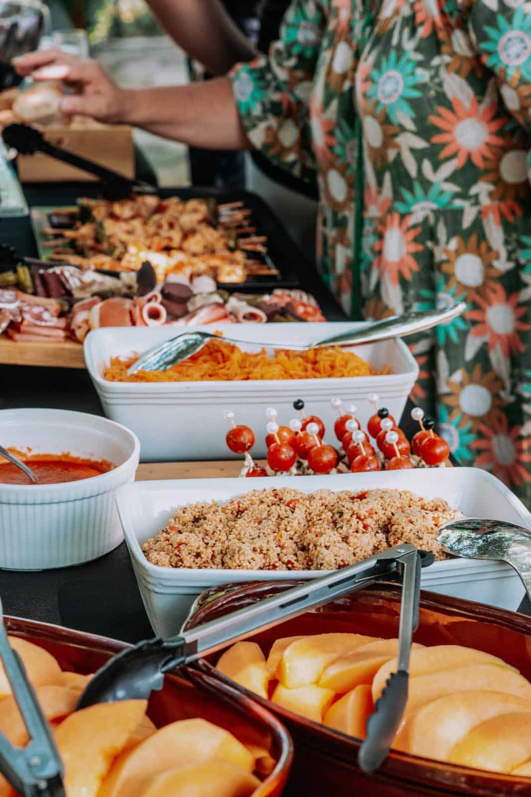 Buffet convivial : brochettes grillées, salade de couscous, tomates cerises et melon frais découpé.