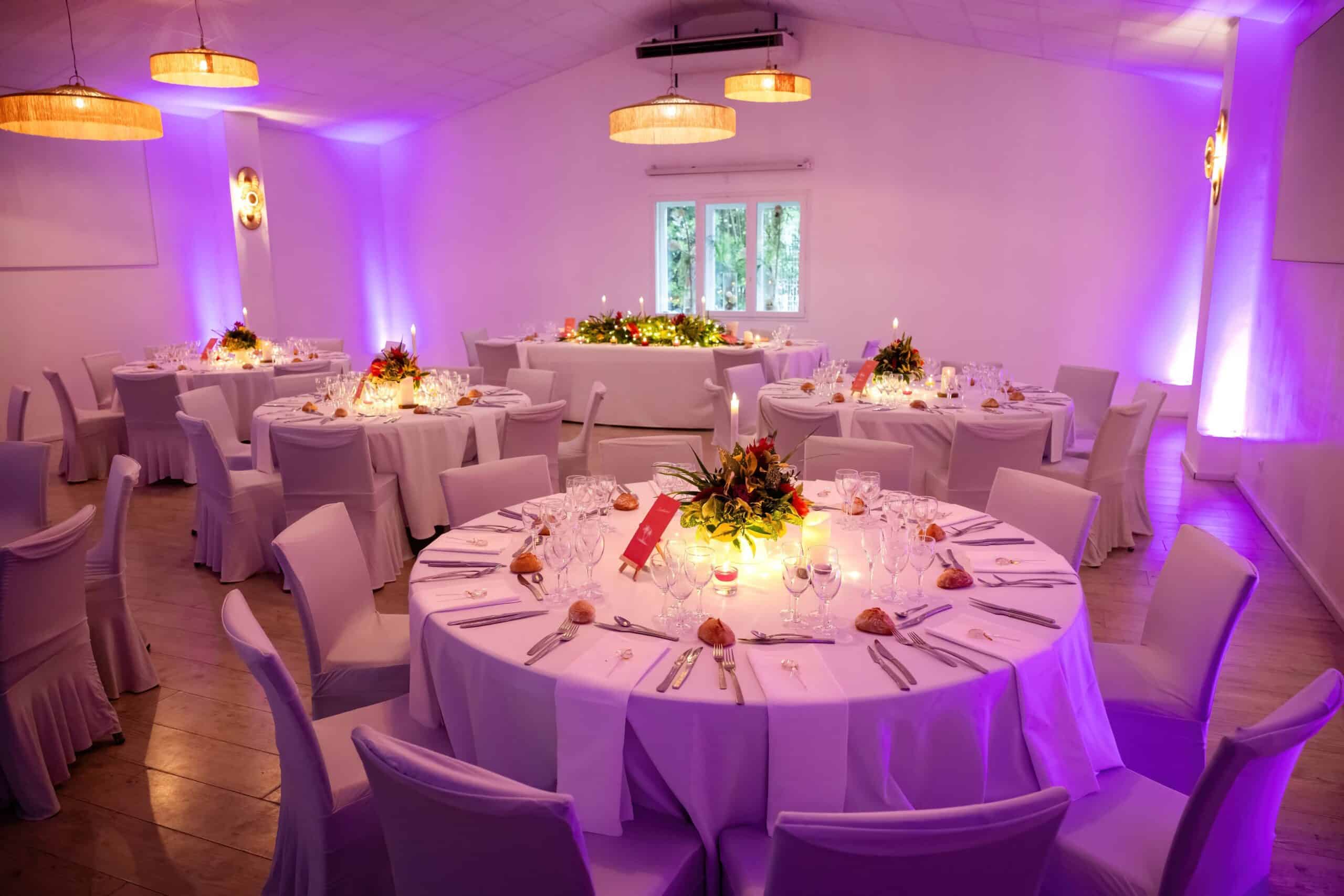 Salle de réception élégante avec tables rondes fleuries et éclairage d'ambiance violet pour un banquet chic.
