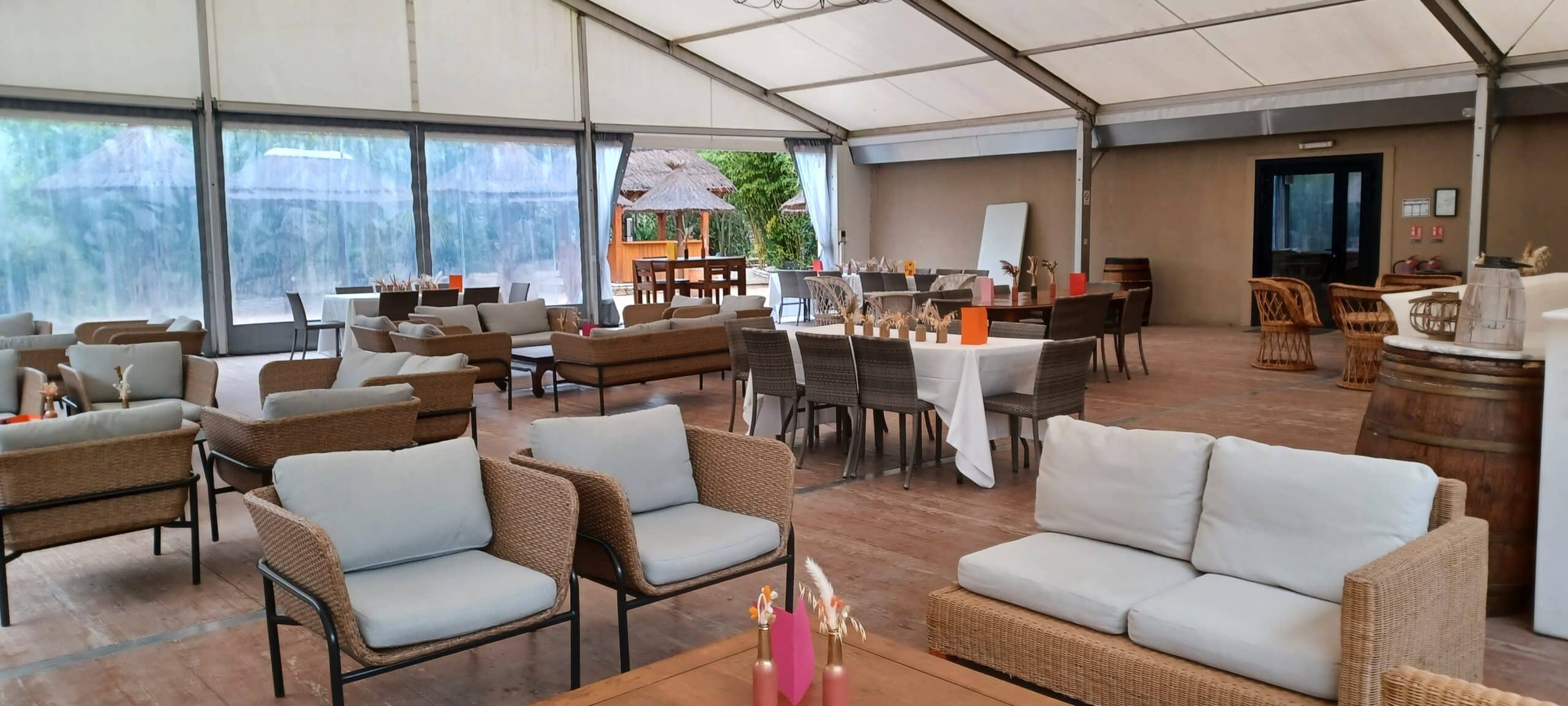 Salon lounge et espace de réception sous chapiteau avec mobilier en rotin, fauteuils gris et tables de banquet.