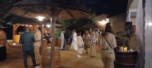 Invités discutant lors d'un cocktail nocturne sous des paillotes exotiques avec tonneaux de vin.