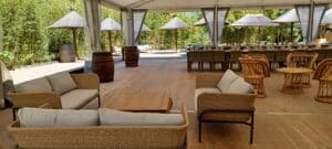 Salon de jardin en osier avec canapés gris, tonneaux décoratifs et paillotes sous une tente de réception.