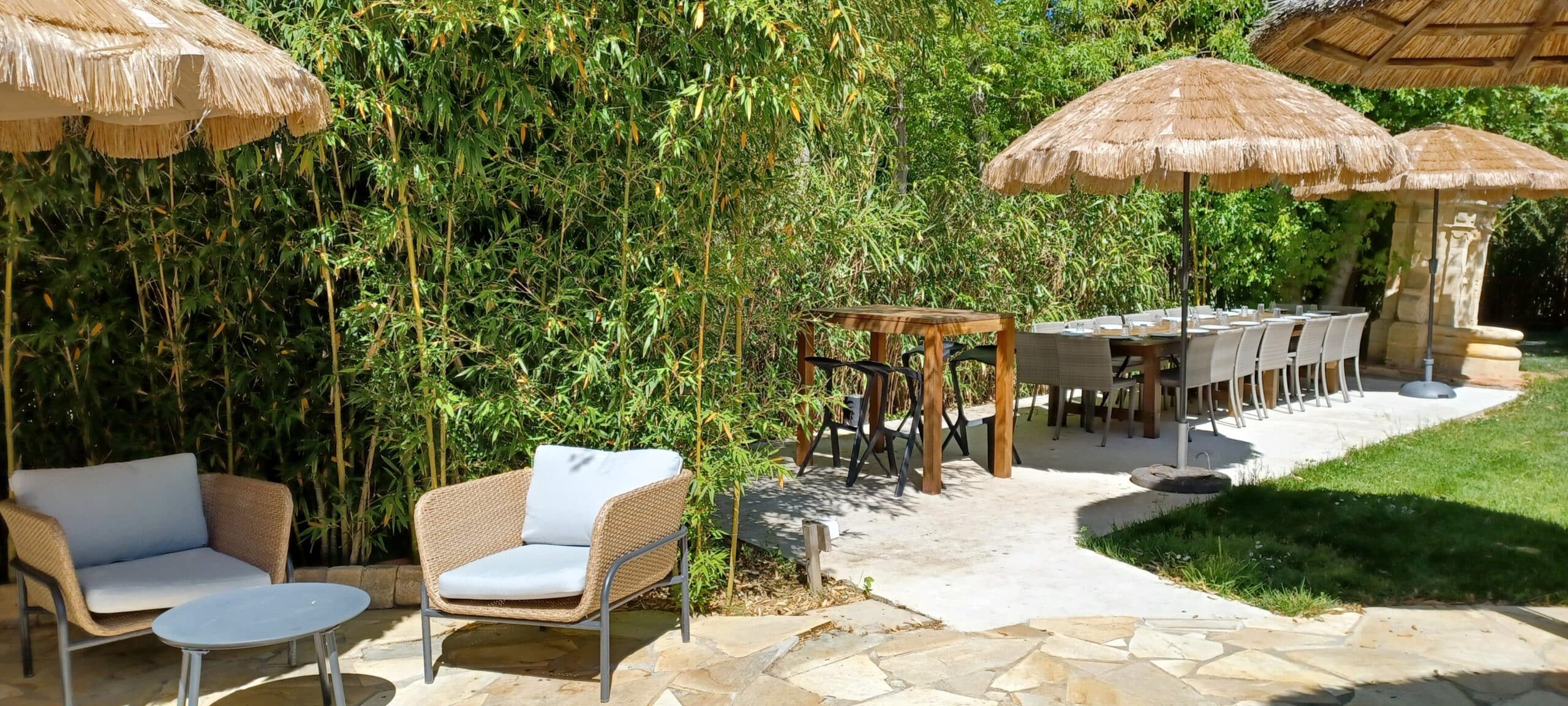 Terrasse ensoleillée avec fauteuils en rotin, parasols en paille et bambous pour une ambiance tropicale relaxante.